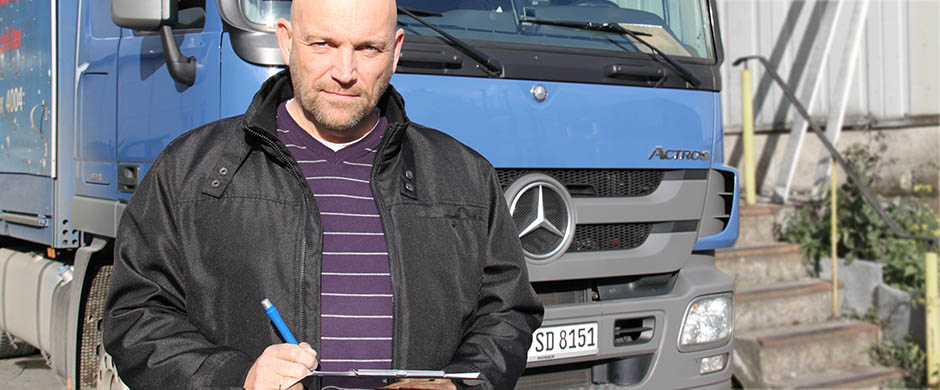 Ein Gefahrgutfahrer steht vor einem blauen LKW und notiert etwas auf seinem Notizbrett