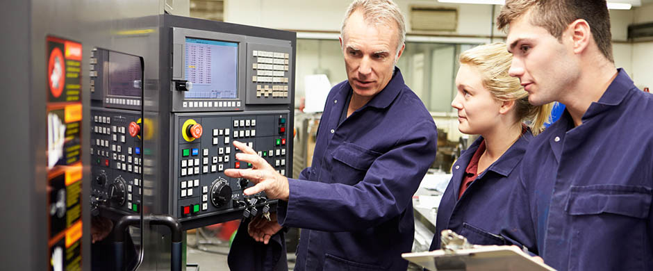 Ein Fachmann erklärt zwei Mitarbeitenden die Funktionsweise einer CNC-gesteuerte Werkzeugmaschine